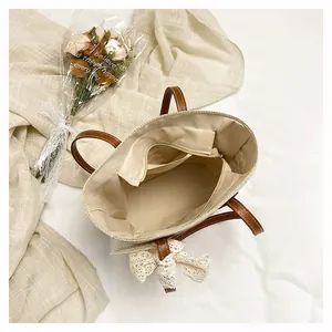Woven straw tote bag interior showing beige fabric lining, zipper pocket, and chic lace bow accent.