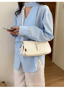 Détail d'un sac sous le bras crème chic avec breloque cheval porté par un mannequin
