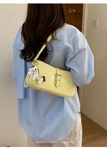 Modèle portant un sac sous les bras jaune avec un charm de cheval et chaîne de perles