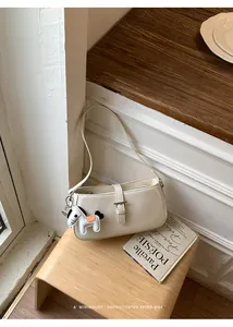 Détail d'un sac baguette blanc crème avec un charmant pendentif cheval sur tabouret.