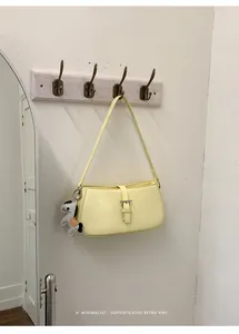 Détail du sac à épaule jaune minimaliste et élégant suspendu sur un crochet mural.