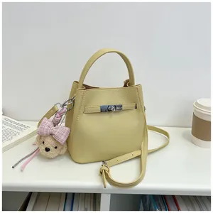 Bolso de mano amarillo tipo cubo de cuero granulado con cierre de metal y peluche mono.