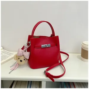 Detalle de un elegante bolso cubo de cuero rojo con un adorable oso de peluche colgante.