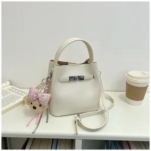 Elegante bolso bombonera blanco crema con correa metálica y un lindo amuleto de oso