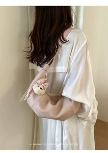 Stylish pink croissant shoulder bag with cute bear pendant, perfect for daily commuting.