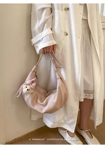 Detailed lifestyle view of a soft pink crescent shoulder bag featuring a cute bear plush charm