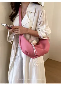 Detail view of the trendy pink croissant slouchy crossbody bag featuring a cute bear plush charm.
