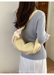 Detailed view of fashionable yellow leather croissant shoulder bag with cute plush bear charm.