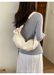 Casual PU leather croissant shoulder bag with cute plush bear pendant for women daily commuting.