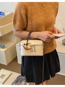 Detailansicht einer cremeweißen Handtasche mit Pferdeanhänger und Kettenriemen