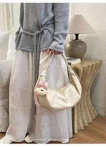 Detail shot of creamy white crescent shoulder bag with cute bear charm and stylish pleats.