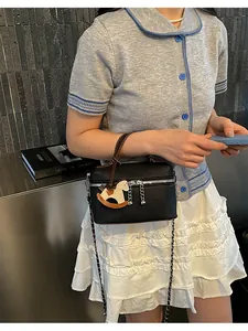 Detailansicht einer schwarzen strukturierten Handtasche mit einem Schaukelpferd-Anhänger.