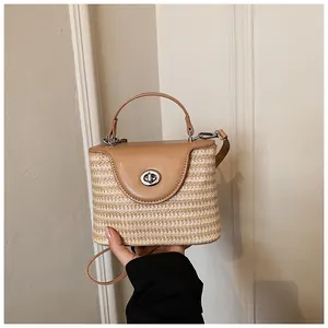 Détail d'un sac seau en paille tissé main avec rabat en cuir, tenu à la main par le sujet