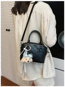 Detail view of a black fashion crossbody bag with cute plush pendant and embossed pattern.