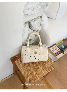 Bolso de lunares crema con lazo y dije de corazón sobre un taburete de madera tejido