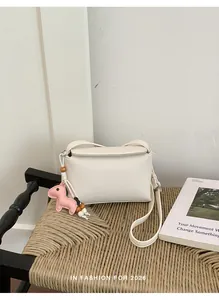 Borsa a tracolla bianca martellata con ciondolo rosa su una sedia intrecciata sobria