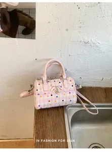 Primer plano de un bolso rosa con lunares y cuadros vichy sobre una mesa de madera.