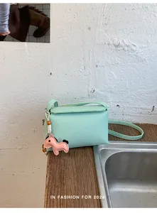 Dettaglio borsa a tracolla verde menta in pelle martellata con charm pony rosa.