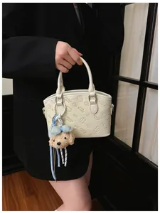 Close-up detail of beige fashion shoulder bag with debossed cat pattern and cute plush charm.