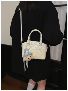 Detail view of trendy cream shoulder bag featuring cute cartoon debossed patterns and plush charm.