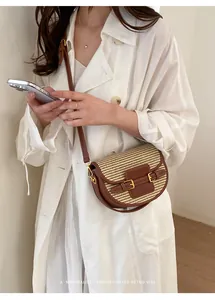 Woven straw saddle bag with brown leather trim shown in a minimalist lifestyle setting