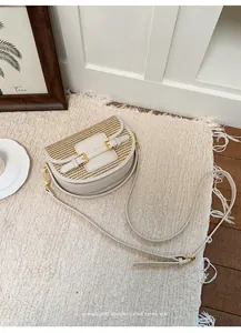Detailed view of woven straw saddle bag with cream leather trim and gold buckles