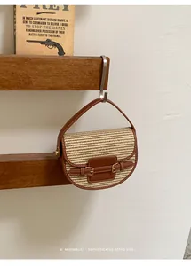 Detailed view of a woven straw saddle bag with brown leather trim hanging on a hook