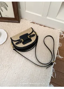 Elegant straw woven saddle bag for women featuring black leather trim and gold buckle details