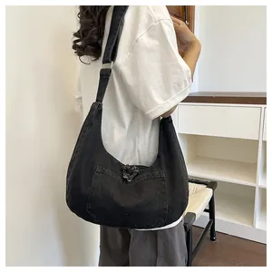 Detailed side view of a large black denim crescent hobo bag with a wide strap