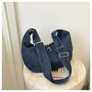 Close-up perspective of a dark blue denim hobo bag on a minimalist white stand
