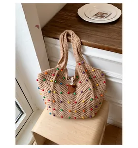 Primer plano de un gran bolso de playa de paja con cuentas de colores en un taburete de madera.