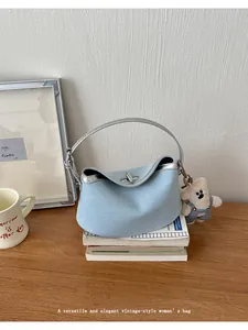 Detailed view of trendy denim shoulder bag with metallic trim and cute plush bear charm.