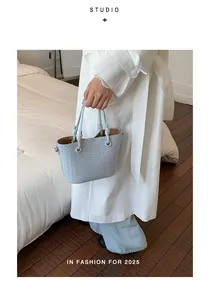 Close-up of light blue woven bucket bag held by a person in a white trench coat