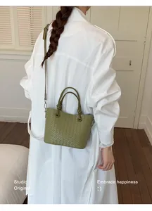 Elegant green woven handbag styled with a long white coat for a minimalist chic look