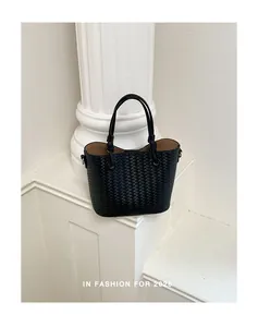Black woven leather bucket bag with handle detail in a minimalist white studio setting