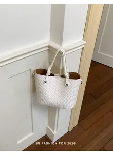 Detail shot of a white woven bucket bag hanging on a minimalist white wall corner.