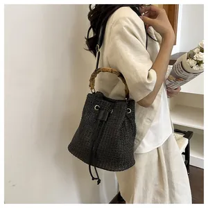 Vue détaillée du sac seau tressé noir doté d'une poignée en bambou naturel et cordon.