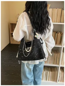 Dettaglio della borsa a spalla in tela nera con stelle, catene metalliche e perle.
