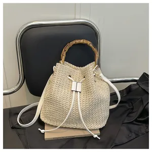 Sac seau en paille tressée pour femme avec poignée en bambou et bandoulière blanche plage.
