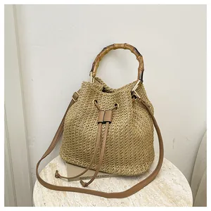 Vue rapprochée du sac seau en paille d'été avec poignée en bambou naturel et bandoulière.