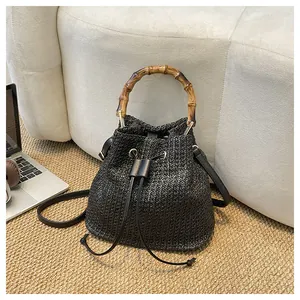 Vue détaillée du sac seau en paille tressée noire avec poignée en bambou naturel et liens en cuir.