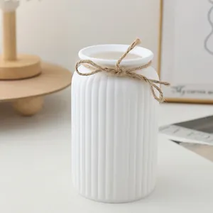 Primer plano del jarrón estriado blanco minimalista con lazo de yute en mesa decorativa.
