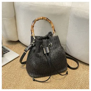 Vue détaillée d'un sac seau en paille tressée noire avec poignée supérieure en bambou naturel.