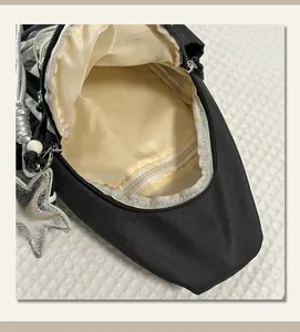 Black nylon chest bag detail view, beige lining inner pocket, silver star pendant charm.