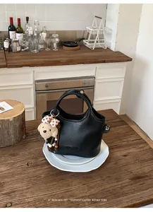Sac seau de banlieue en cuir noir avec un joli charme d'ours sur une table en bois