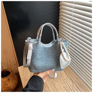 Detailed view of a small blue denim handbag featuring a heart-shaped pearl bag charm