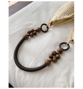 Detailed view of the dark brown wooden bead and rope strap on a beige woven beach bag