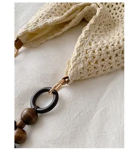 Close-up of cream crochet beach bag texture and wooden bead shoulder strap detail.