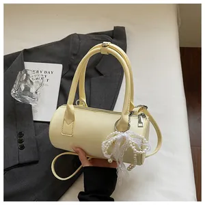 Detail of a chic cream yellow cylinder handbag featuring a pearl and lace bow charm.