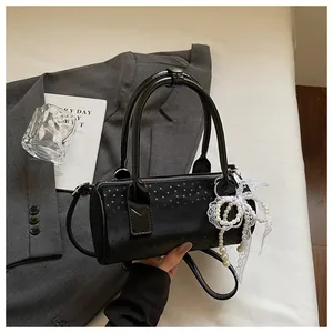 Close-up detail of a chic black cylindrical handbag with pearl and lace bow charm decor